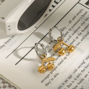 Macro view of cherry-shaped gold pendant and silver hoop earrings on a vintage paper