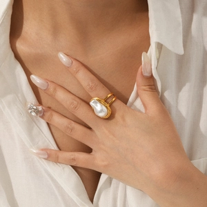 Gros plan d'une bague perle baroque irrégulière avec double anneau doré sur un doigt