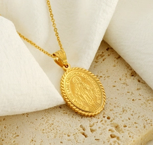 Macro detail of a gold oval religious medal necklace on textured beige stone background