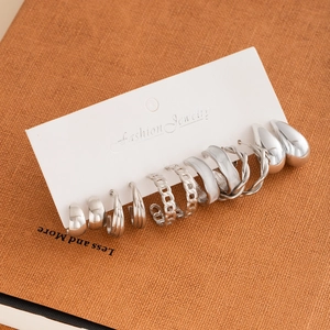 Silver earring set with C-shaped hoops and studs displayed on a card with a leather backdrop