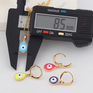 Detailed measurement of golden teardrop evil eye pendant showing 8.5 mm width on a caliper