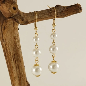 Détail de boucles d'oreilles dorées 18k avec trois perles blanches dégradées sur branche