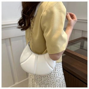Close-up of white pleated half-moon bag with metal chain strap on woman shoulder