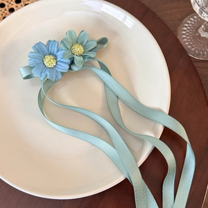 Detail of light blue daisy fabric flowers with long ribbons on a ceramic plate