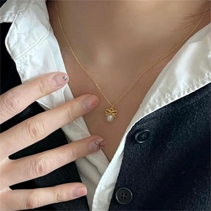 Detail of a golden bow necklace with a white pearl pendant on a female model