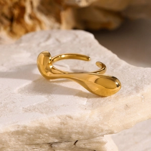 Detailed shot of an irregular gold water-drop ring resting on a white textured rock surface