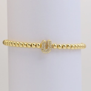 Detail of gold bubble letter U charm with micro-pave cubic zirconia on beaded bracelet