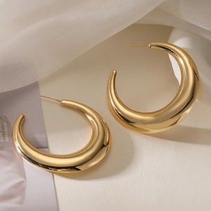 Detail of chunky gold-plated C-shape hoop earrings on minimalist textured background