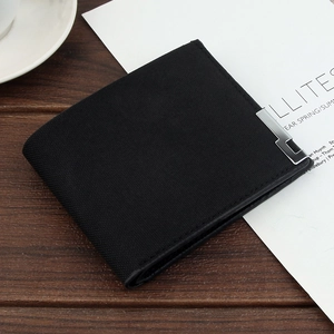 Short black bifold men wallet with silver metal trim on textured fabric on wood background