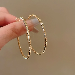 Macro shot of large golden hoop earrings with unique segmented bamboo-like texture