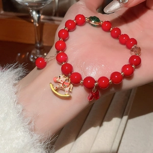 Detail of red beaded bracelet with gold accents and a painted rocking horse charm
