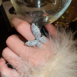 Close-up of elegant butterfly ring with sparkling zircons worn while holding a glass