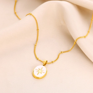 Macro shot of gold oval necklace pendant featuring starburst design on beige fabric