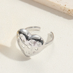Close-up of silver hollow heart-shaped adjustable ring on a textured stone surface