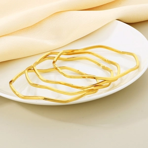 Detailed view of four wavy gold titanium steel bangles stacked on a white ceramic plate