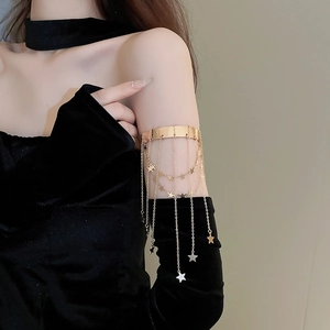Detail of a gold metallic arm cuff with star pendant tassels worn on a black velvet sleeve