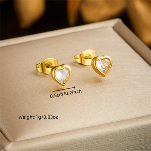 Elegant gold heart stud earrings with clear zirconia on a beige textured jewelry box