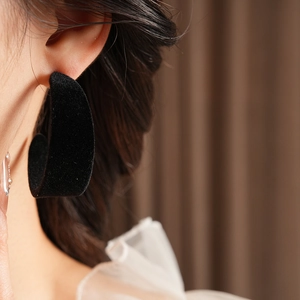 Close-up of black flocked C-shaped earrings with velvet texture on a model side profile