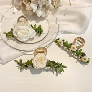 Detailed macro view of gold floral hair claws with white roses and green fabric leaves