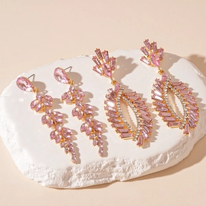 Elegant gold earrings with pink crystals and rhinestones displayed on a white stone