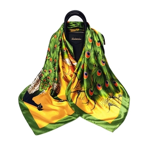 Elegant peacock print silk scarf draped over a black bag against a clean white background