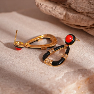 Detailed close-up of retro gold-plated drop earrings with red resin and black enamel