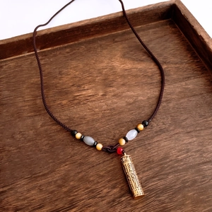 Close-up of golden mantra cylinder pendant with multi-color beads on wooden tray