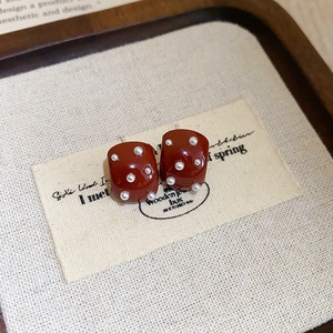 Détail de boucles d'oreilles carrées rouges avec perles blanches sur plateau en bois rustique