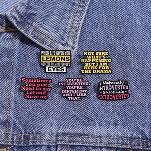 Close-up of five colorful enamel quote pins styled on a blue denim jacket pocket