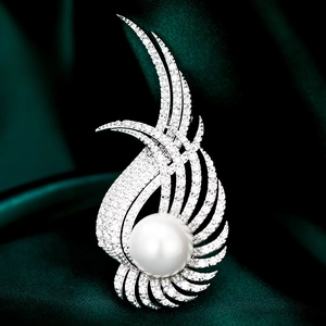 Détail macro d'une broche en perle de luxe avec ailes en zircon sur velours vert