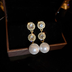 Macro shot of gold pearl drop earrings with micro-paved crystals in a velvet jewelry box