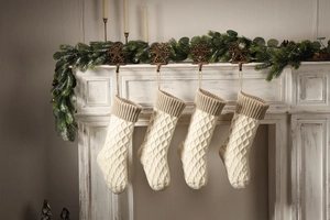 Nahaufnahme von vier grob gestrickten Weihnachtsstrümpfen an einem Kaminsims