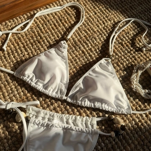 Detail of white bikini set with decorative brown beads and shell ornaments on straw mat