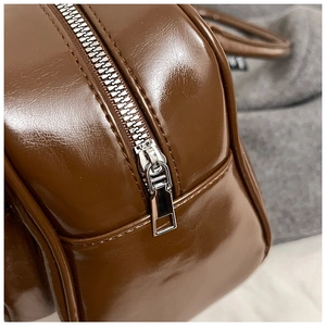 Detail of silver zipper and reinforced stitching on dark brown glossy leather pillow bag