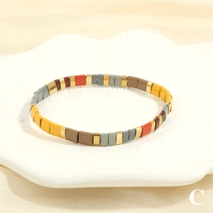 Macro shot of colorful Tila tile beads in matte gold and deep grey on a white petal tray