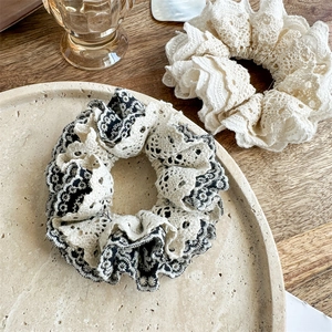 Close-up of layered hollow lace scrunchies in black and cream on a ceramic tray