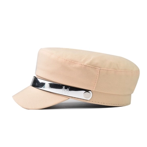 Detail of beige flat top cap with silver metallic band and embossed M letter ornament