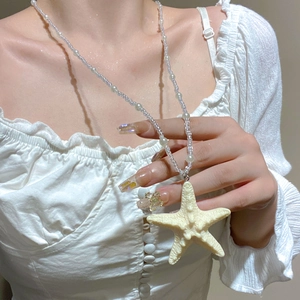 Close-up of a white starfish pendant on a beaded necklace worn by a female model