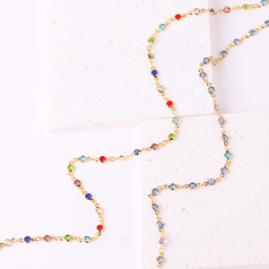 Detail of gold-plated necklace with vibrant multi-colored zircon stones on white stone