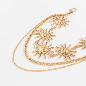 Detail of layered gold chain body belt featuring embossed sun face charms and lobster clasp
