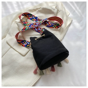 Detail of black canvas bucket bag with colorful geometric strap and tassel fringe