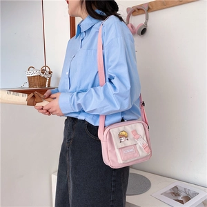 Detail of pink and white canvas crossbody bag featuring cartoon girl pin and fabric label