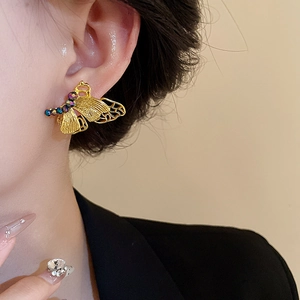 Macro detail of butterfly earring featuring brushed gold finish and iridescent gemstone