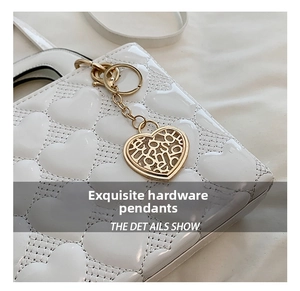 Close-up detail of a white heart-quilted handbag featuring a gold heart-shaped charm