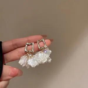 Détail de boucles d'oreilles dorées avec pétales blancs et accents de gemmes