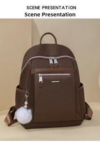 Detail of dark brown nylon backpack with silver zippers, side pocket and white fur pompom