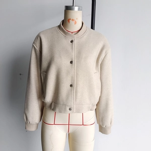Close-up of beige tweed bomber jacket featuring ribbed collar and metal snap buttons