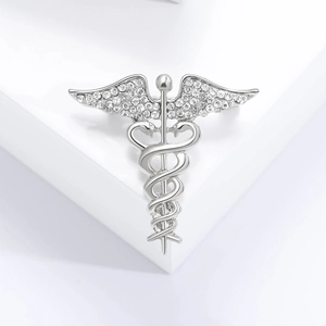 Detailed macro of silver winged caduceus brooch with inlaid rhinestones on a white stand