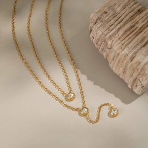 Close-up of a double-layer gold necklace with round zircon inlays next to a raw stone