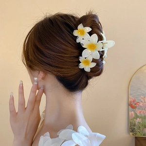 Macro detail of acrylic plumeria flower hair claw clip on model hair for summer styling